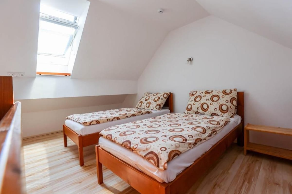 Un piccolo alloggio con una singola stanza, soffitto a sbalzo, due letti singoli con biancheria a motivi coordinati, una panca in legno e un tavolino.