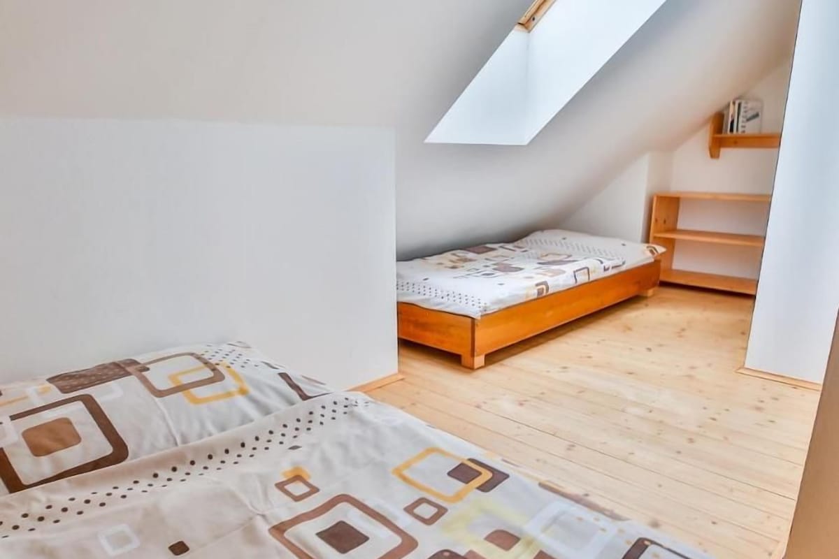 Una camera da letto con soffitto spiovente, un letto di legno, un piccolo comodino e una finestra.
