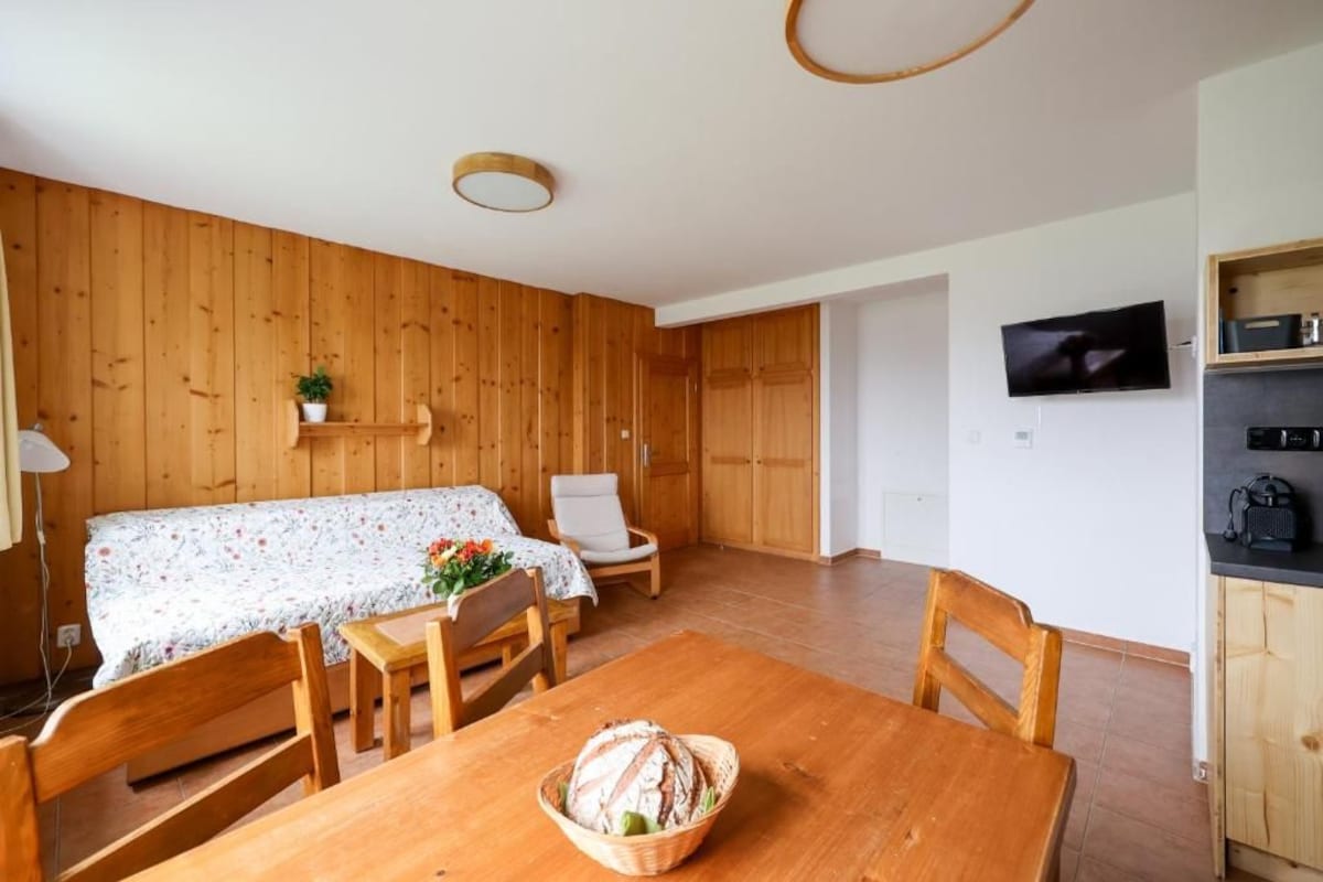 Una stanza con pareti in legno, un tavolo da pranzo con sedie, un televisore a parete e un angolo cottura con mobili.