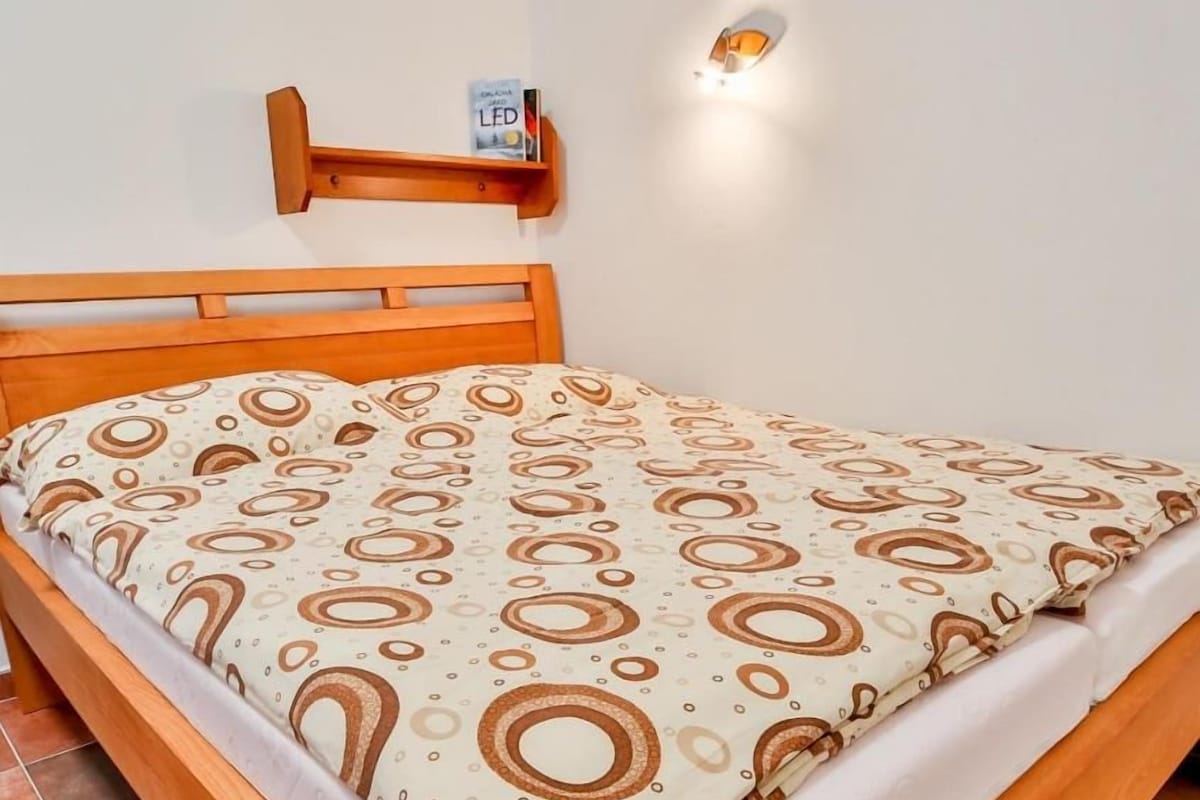 Un letto con copriletto decorato, una testata in legno e uno scaffale a parete con un piccolo oggetto.