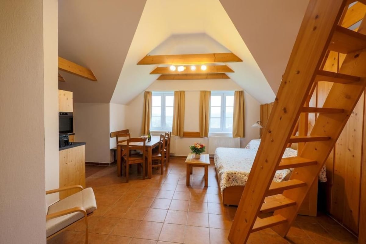 Una stanza compatta con zona pranzo, un letto, una scala in legno e angolo cottura.