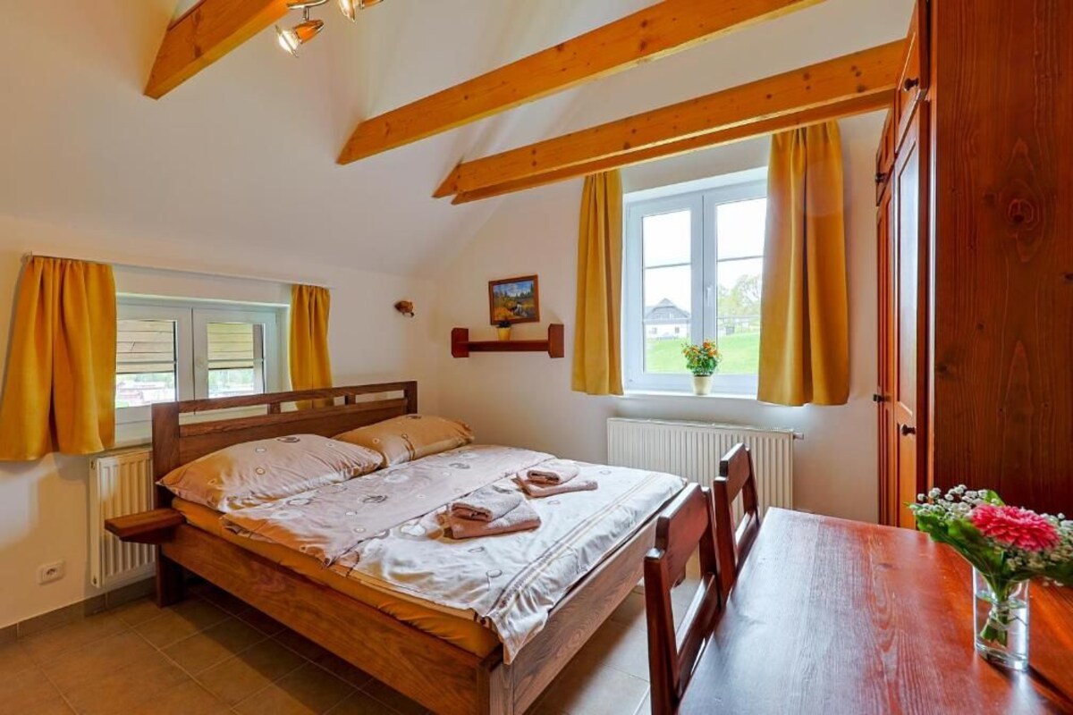 A bedroom with a wooden bed, a wooden table, and a window with curtains.