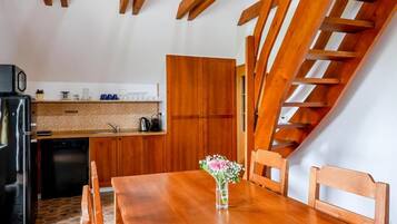 Een houten eettafel met stoelen, een vaas met bloemen, een keuken met houten keukenkastjes en een houten trap.