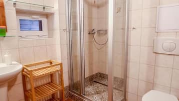 Un bagno con doccia, WC e mobiletto contenitore.