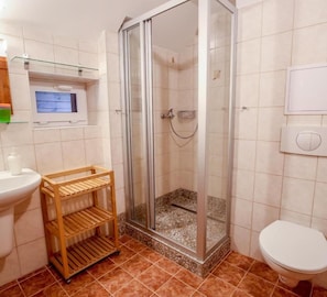 Un bagno con doccia, WC e mobiletto contenitore.