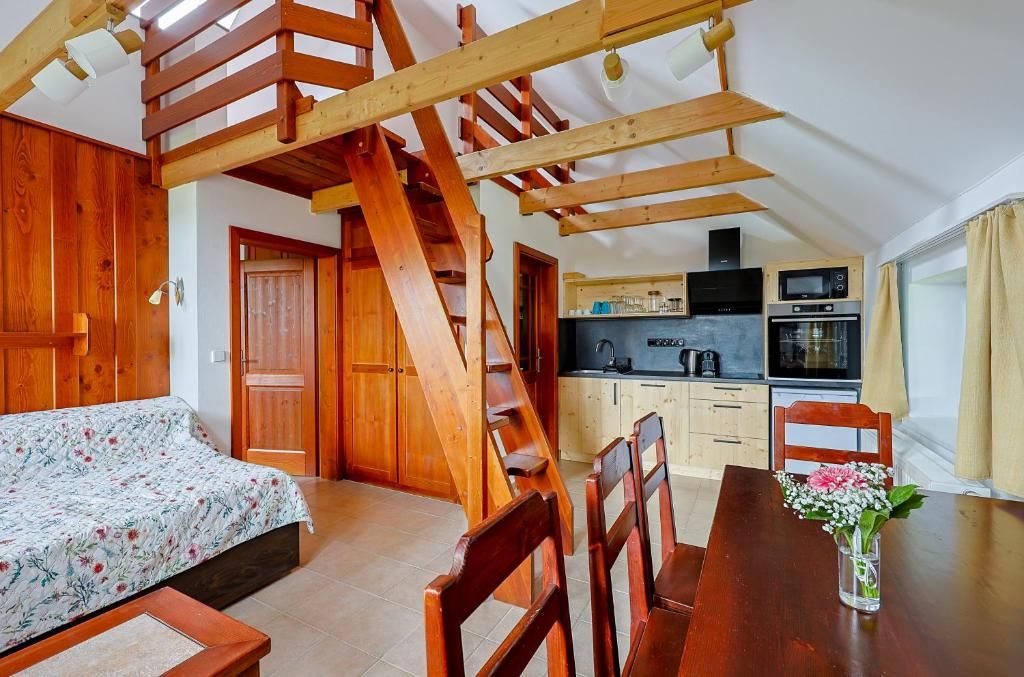 A bedroom with a wooden staircase, a dining area with chairs, and a kitchen with appliances.