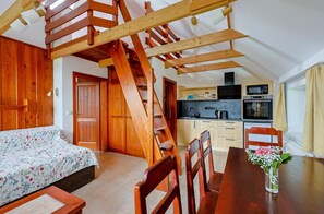 A bedroom with a wooden staircase, a dining area with chairs, and a kitchen with appliances.