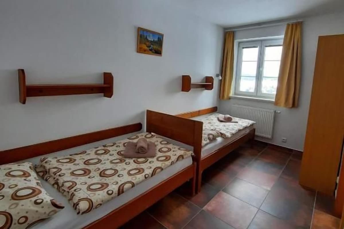 Una stanza con due letti singoli, una piccola finestra con tende e un termosifone.