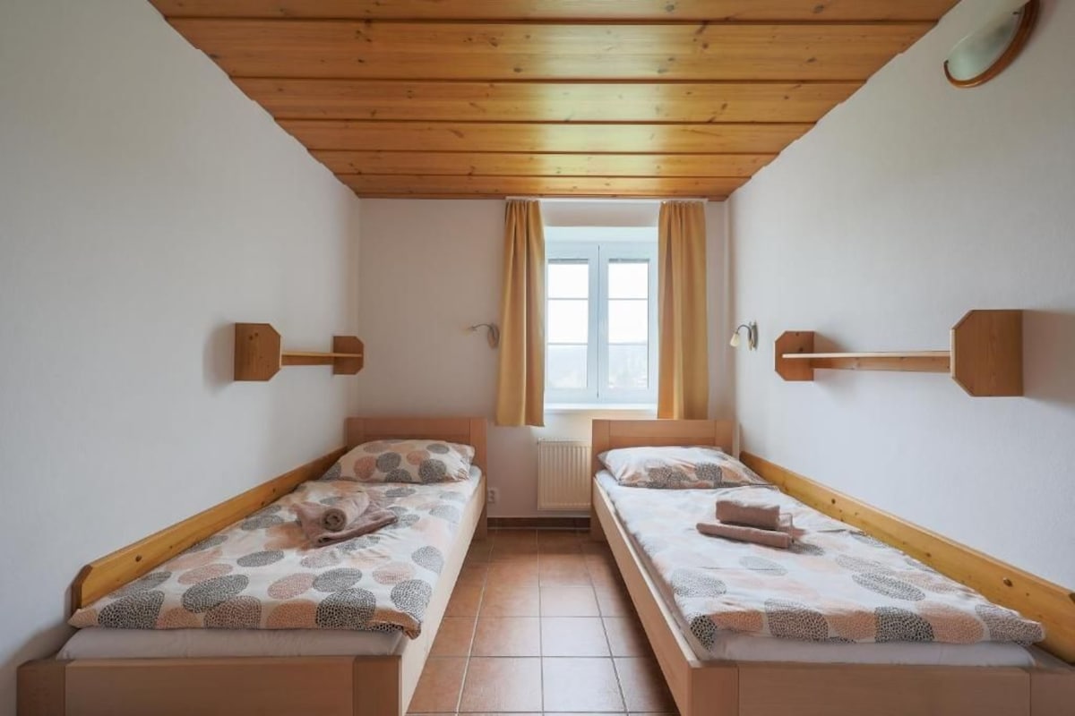 Una stanza con due letti a castello in legno, una finestra con tende e un termosifone.