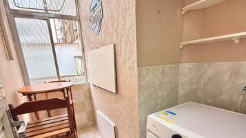 A laundry room with a washing machine, a drying rack, and a chair.