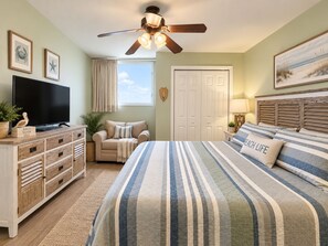 Une chambre à coucher comprenant un lit, un téléviseur, un ventilateur de plafond, une commode, une fenêtre et une porte.