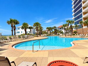 A pool area with lounge chairs and palm trees, surrounded by buildings. - Luxury Coastal Condo, Pool, Hot Tub, 11th Floor (Panama City Beach)