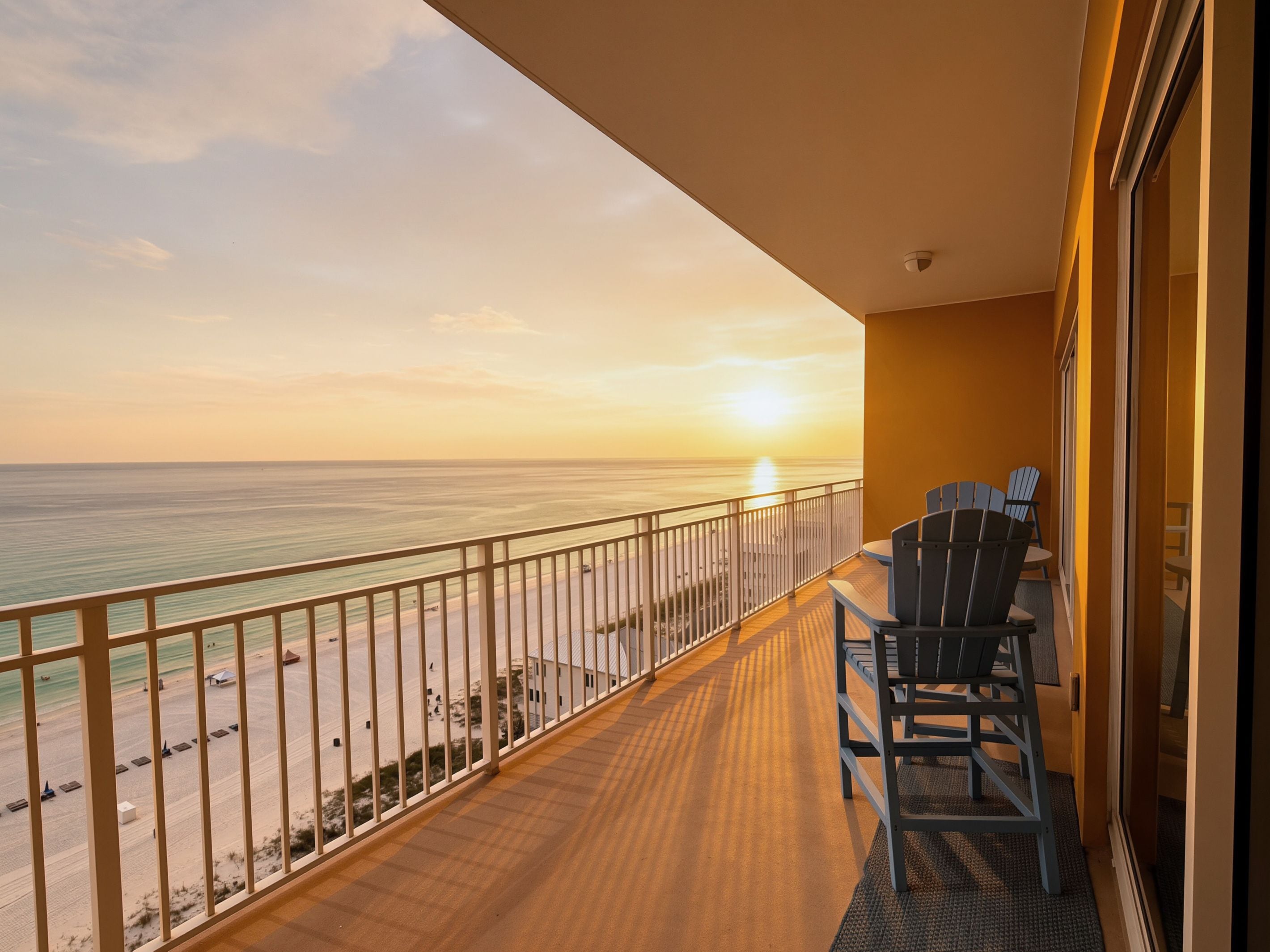 A balcony with a view of the ocean and a sunset. There are two chairs and a table on the balcony.
