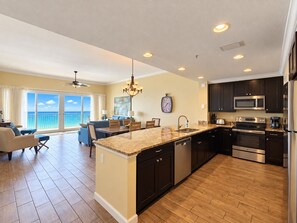 A modern kitchen with a central island, dark cabinetry, stainless steel appliances, and a view to the outside. - Luxury Coastal Condo, Pool, Hot Tub, 11th Floor (Panama City Beach)