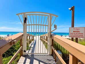 A beach access gate with a notice sign, wooden railings, and a clear view of the beach. - Luxury Coastal Condo, Pool, Hot Tub, 11th Floor (Panama City Beach)