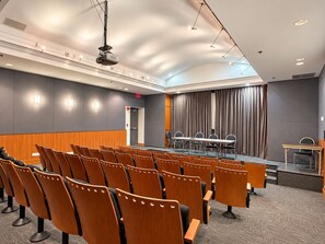 Konferenssihuone, jossa on riveissä tuoleja, pitkä pöytä ja projektori.