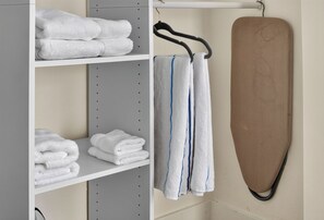 Un espace de rangement avec des étagères où sont pliés des serviettes, et un fer à repasser marron appuyé contre le mur.