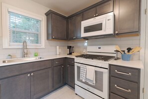 Una cocina moderna con armarios de madera oscura, un lavamanos de acero inoxidable, un microondas, una estufa a gas y un horno.