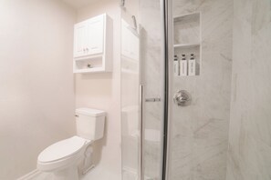 Une salle de bain équipée de toilettes, d’une douche à parois de verre et d’une étagère contenant des articles de toilette.