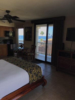 A hotel room with a bed, a dining table, chairs, a kitchen area, a balcony with a view of the ocean, and a television. - New Lahaina Shores 5th Floor  2 Lanai's Ocean view & Mountain View Corner unit (Lahaina)