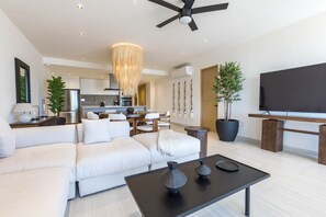 A modern living room with a sectional sofa, a coffee table, a TV, and a dining area in the background. - Pedregal Horizon | Views & Private Beach Access (Cabo San Lucas)