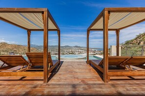 Eine Holzterrasse mit zwei Liegestühlen und einem Pool im Hintergrund.