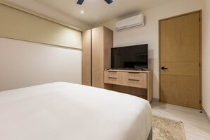 A bedroom with a bed, a wooden wardrobe, a television, and an air conditioning unit. - Pedregal Horizon | Views & Private Beach Access (Cabo San Lucas)