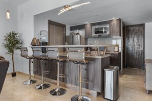A modern kitchen with a central island, bar stools, stainless steel appliances, and a potted plant. - Vista La Jolla 408 | 2BR Suite Ocean View (San José del Cabo)