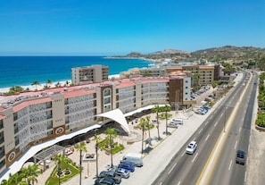 Un hôtel en bord de mer, avec plusieurs étages, une cour intérieure agrémentée de palmiers et une vue sur l’océan.