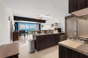 A modern kitchen with a central island, a dining area with a view, and a balcony. - Vista La Jolla 408 | 2BR Suite Ocean View (San José del Cabo)