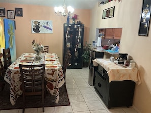 Un coin repas avec une table dressée pour quatre personnes, un réfrigérateur et un espace cuisine comprenant un évier et une cuisinière.