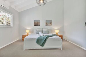 A bedroom with a white bed, two bedside tables with lamps, a window with blinds, and two wall-mounted pictures. - Moreton Bay Acreage Retreat Pool & Fireplace (Ransome)