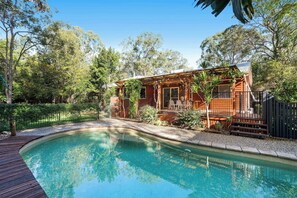 Eine Holzhütte mit Swimmingpool, umgeben von Bäumen und einem eingezäunten Garten.