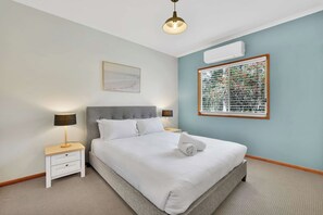 Ein Hotelzimmer mit Bett, Nachttischen, einer Lampe, einer Klimaanlage und einem Fenster mit Jalousien.