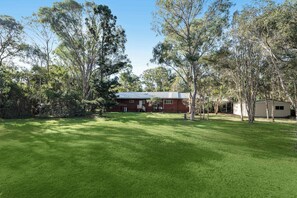 Un bâtiment rouge avec un toit en métal, entouré d’une cour verdoyante et d’arbres.