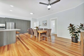 A modern kitchen with grey cabinetry, a stainless steel refrigerator, and a dining area with a wooden table and chairs. - Moreton Bay Acreage Retreat Pool & Fireplace (Ransome)