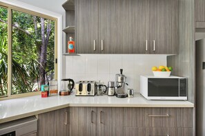 A modern kitchen with a window, cabinets, a coffee maker, a toaster, a kettle, a microwave, and a fruit bowl. - Moreton Bay Acreage Retreat Pool & Fireplace (Ransome)
