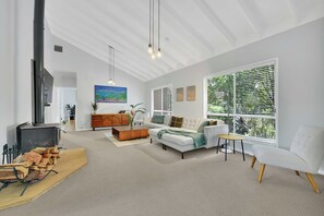A spacious living room with a fireplace, a sofa, a coffee table, and a large window with blinds. - Moreton Bay Acreage Retreat Pool & Fireplace (Ransome)