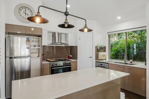 A modern kitchen with stainless steel appliances, a central island, and pendant lighting. - Gold Coast Retreat Theme Parks Nearby (Pimpama)