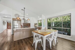 A modern kitchen with a central island, white cabinetry, and a large window offering a view of greenery. - Gold Coast Retreat Theme Parks Nearby (Pimpama)