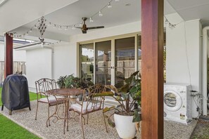 A covered patio area with a table and chairs, a ceiling fan, string lights, and a barbecue grill. - Gold Coast Retreat Theme Parks Nearby (Pimpama)