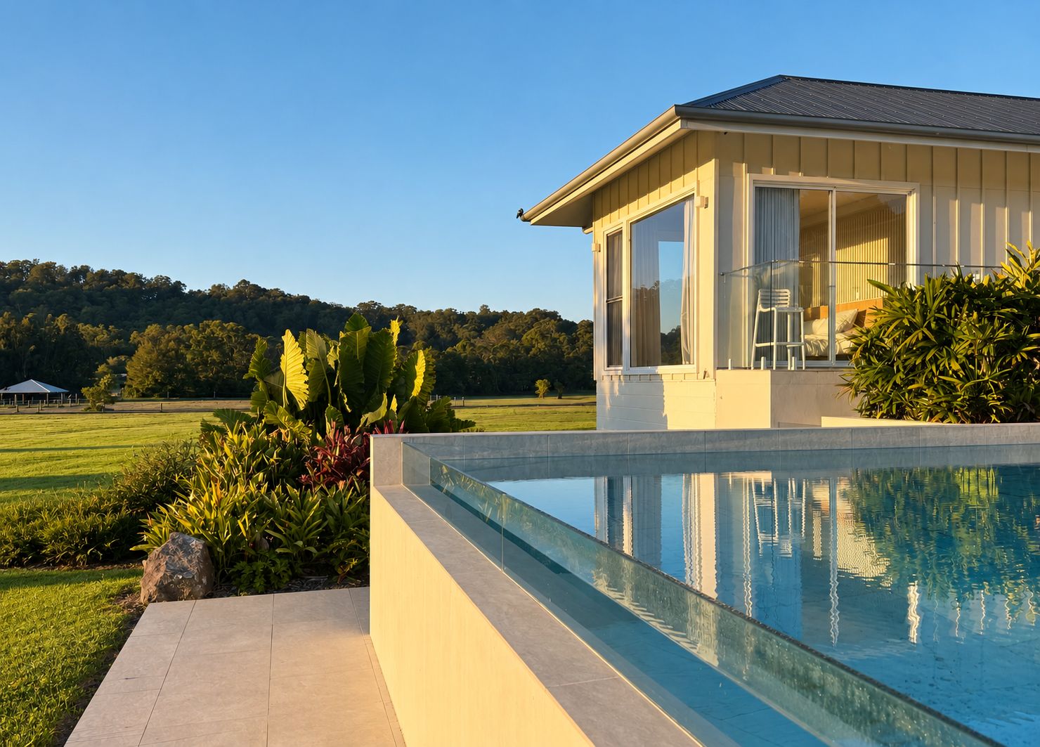 A modern house with a swimming pool, surrounded by lush greenery and a clear view of a distant tree line.