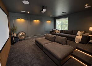 Ein modernes Wohnzimmer mit einem Ecksofa, einem Flachbildfernseher und einem an der Decke befestigten Projektor.