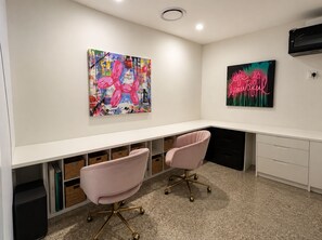 Ein moderner Arbeitsraum mit einem weißen Schreibtisch, zwei rosafarbenen Stühlen und zwei an der Wand befestigten Kunstwerken.