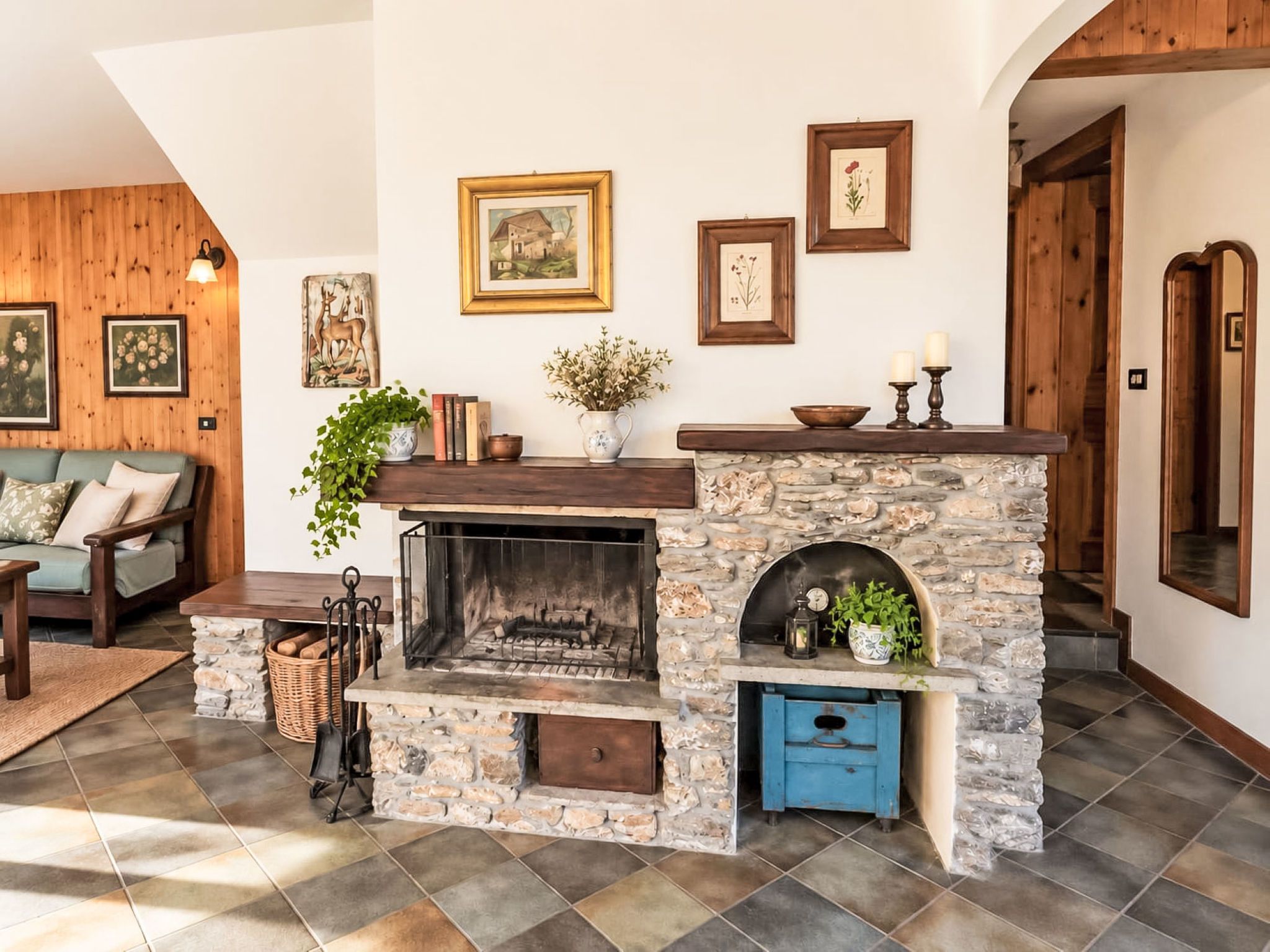 A cozy living room with a stone fireplace, a sofa, and various framed artworks on the walls.