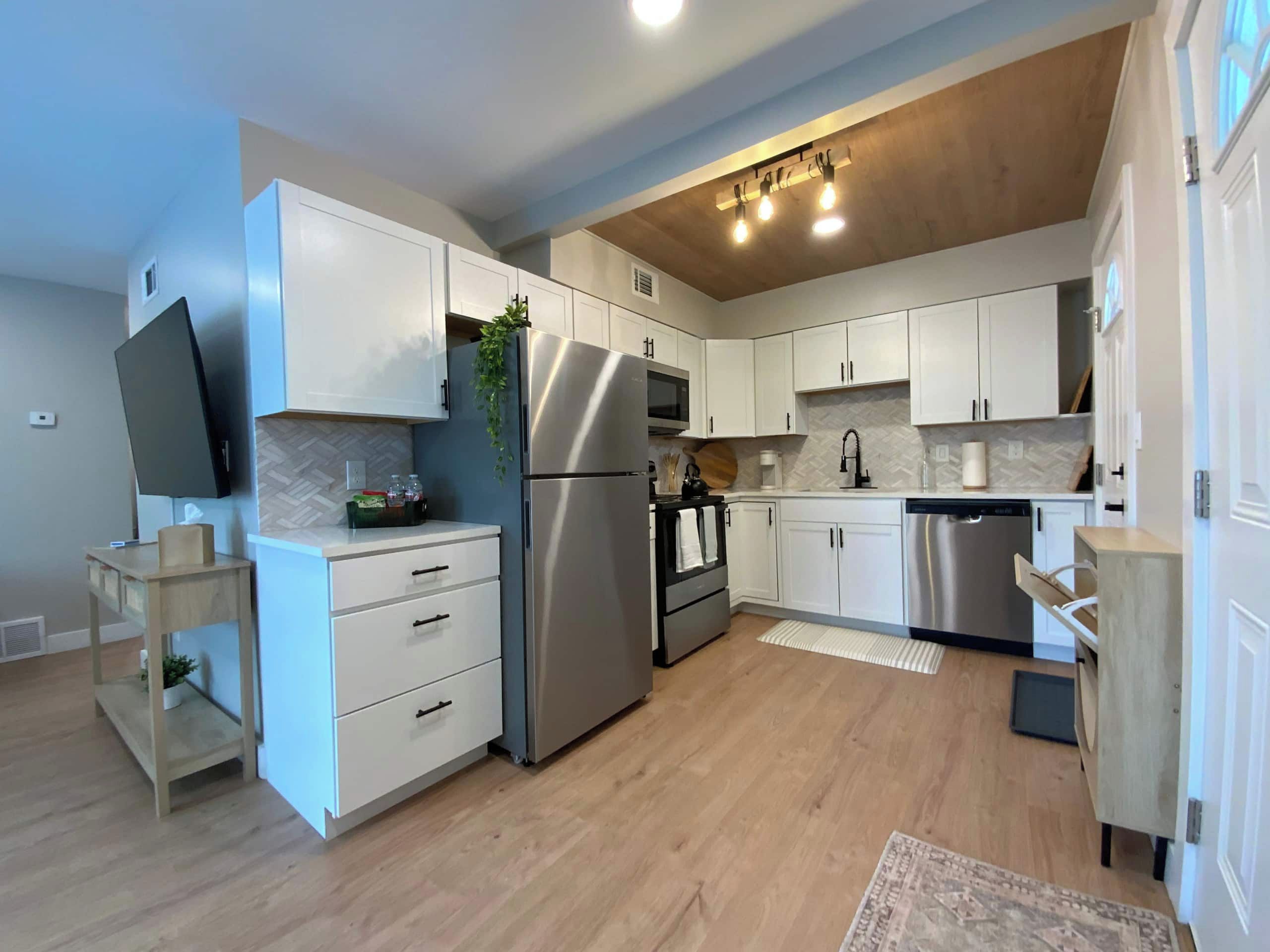 Una cucina moderna con mobili bianchi, elettrodomestici in acciaio inossidabile e soffitto in legno.