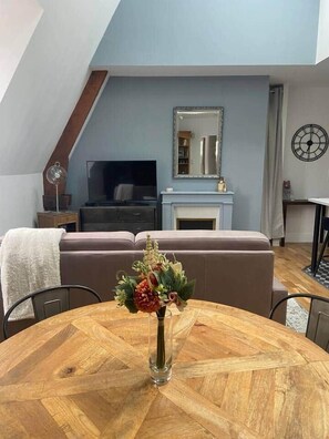 Ein Wohnzimmer mit einem runden Holztisch, einer Couch, einem Kamin und einem Fernseher.