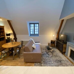 Ein Loft-Zimmer mit einer Couch, Esstisch, Stühlen, einem kleinen Fernseher und einem Kamin.