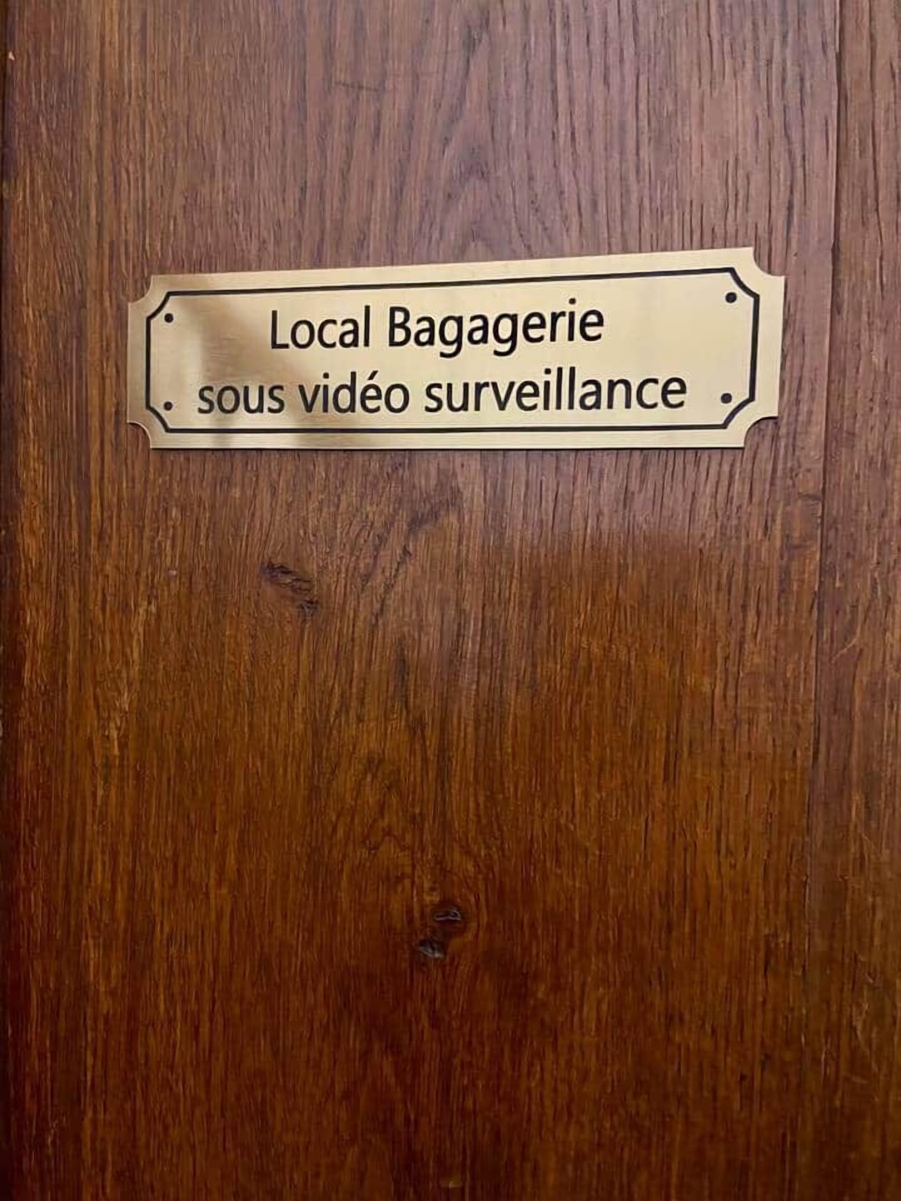 Une porte en bois avec une plaque métallique portant l’inscription : « Bagagerie locale, zone sous vidéosurveillance. »