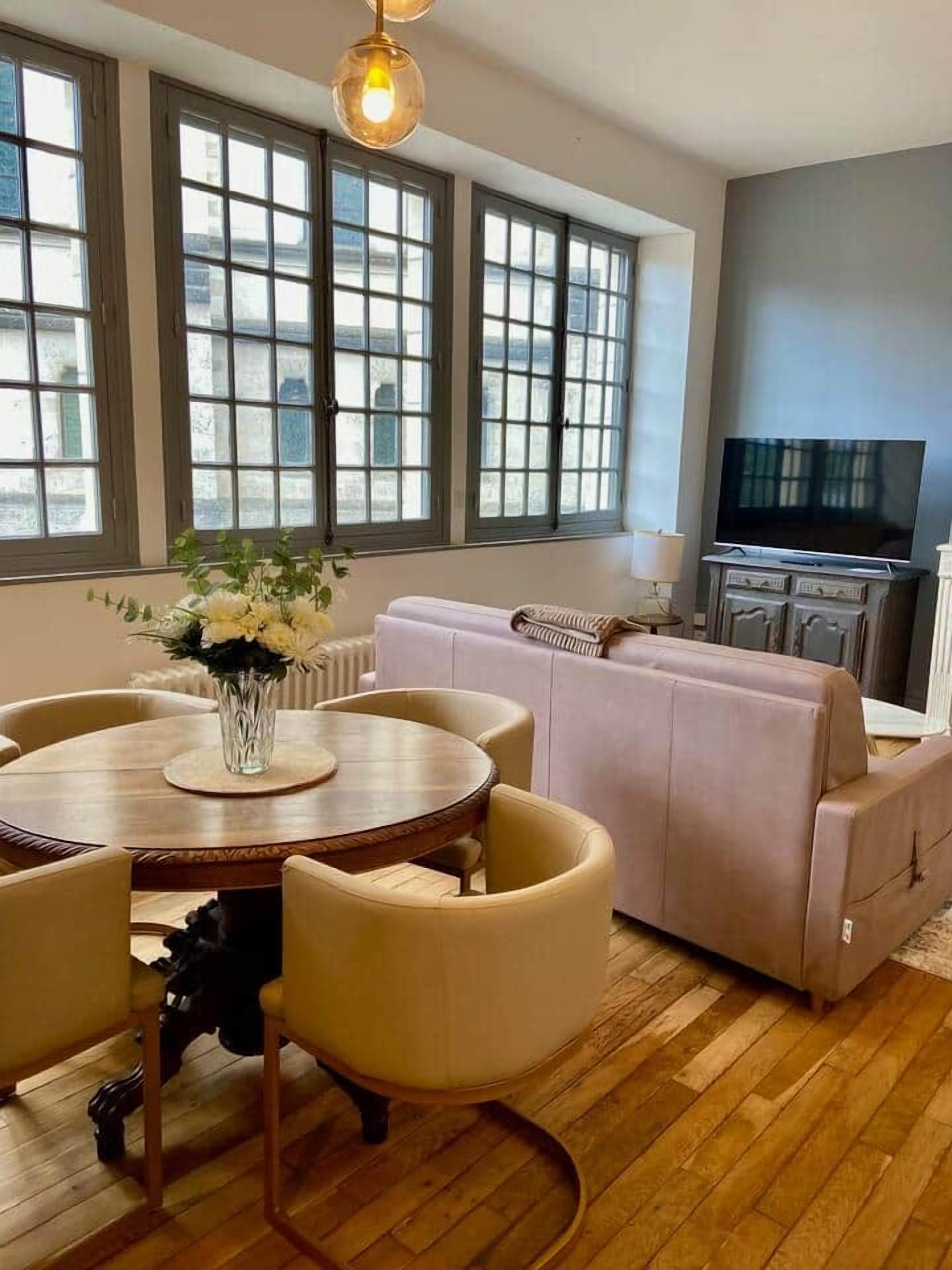 A modern living room with a round dining table, beige chairs, a sofa, and a television.